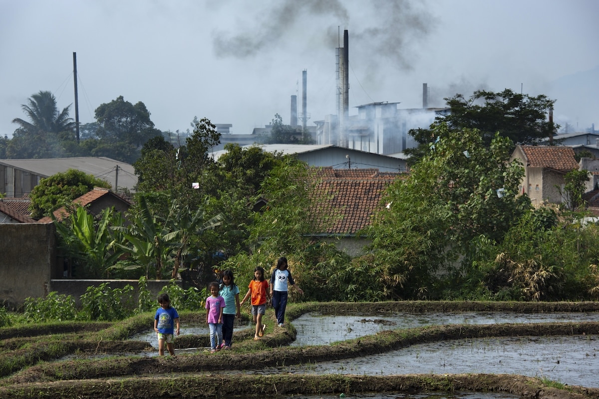 Children walk through a rice paddy near dozens of textile mills which have been using the Citarum River to dump wastewater outside Majalaya, Java, Indonesia