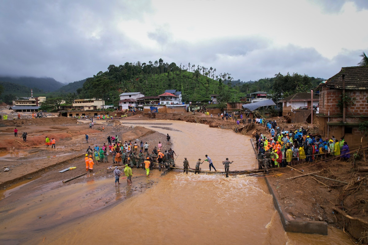 An aerial view shows people crossing a temporary bridge at the site of a landslide in Chooralmala village, India